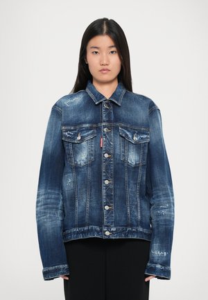 Blå denimjakke med klassisk snit, der har to brystlommer, metalknapper og en slidt tekstur. Lange ærmer og krave detaljer synlige.