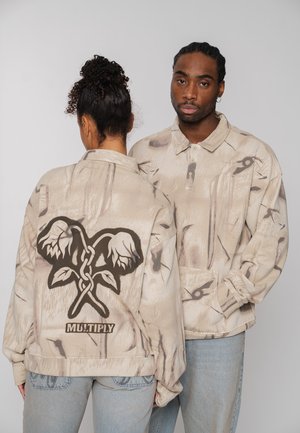 Beige oversized jacket with abstract pattern, featuring a black floral graphic on the back and "MULTIPLY" text near the hem.