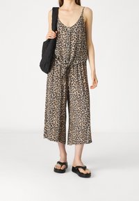 Leopardprint jumpsuit met een v-hals, verstelbare bandjes, een strakke taille en wijde, cropped pijpen. Gekoppeld aan een zwarte, gewatteerde schoudertas.