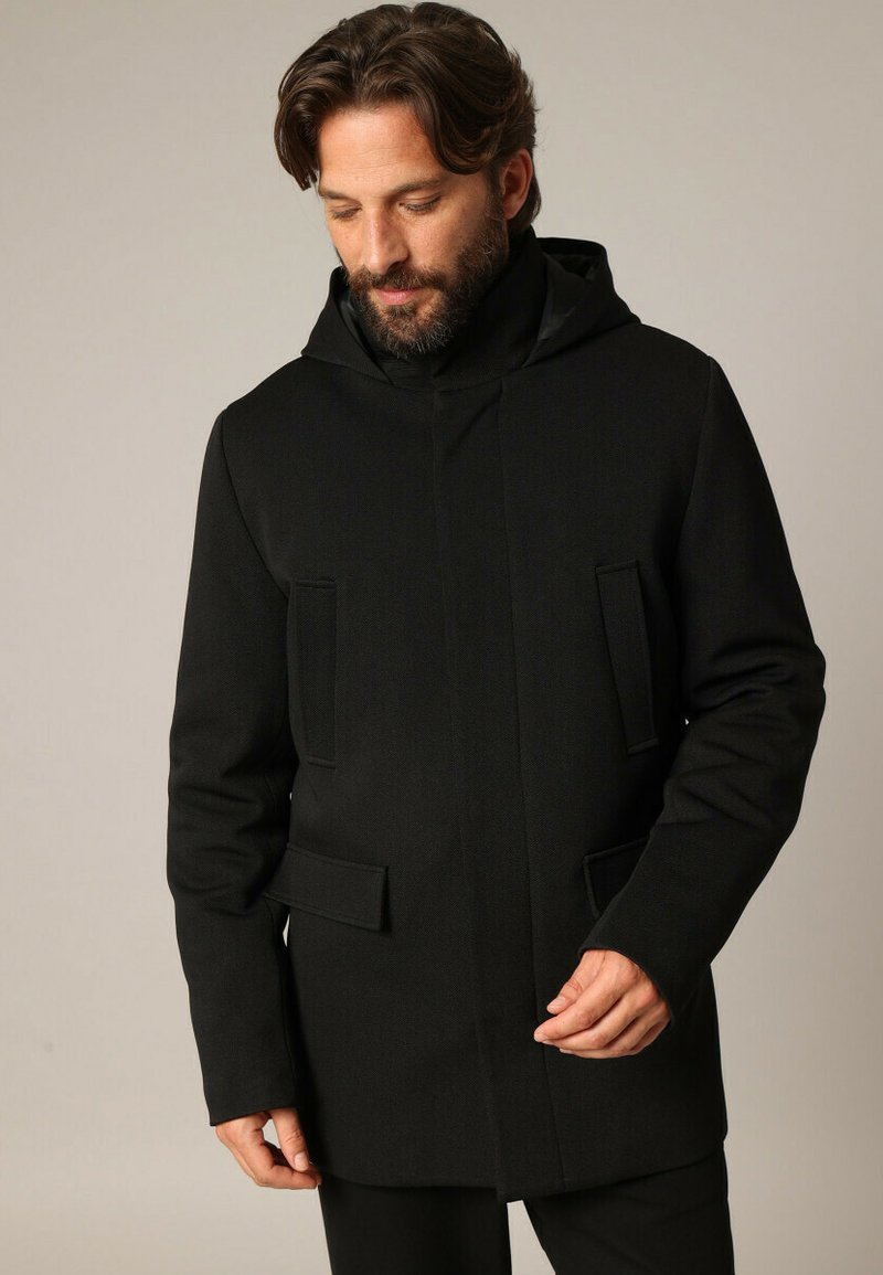 Veste à capuche noire en tissu texturé, dotée de deux poches avant avec fermetures à rabat et d'une silhouette droite.