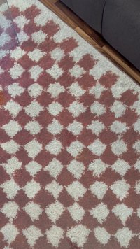 Woven rug featuring a diamond pattern in shades of burgundy and white, with a textured, shaggy surface and a soft, plush appearance.