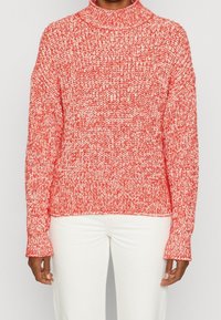 Červeno-bílý pletený svetr s vysokým límcem, volným střihem a žebrovanými manžetami. Textura je objemná a má melírovaný vzor.