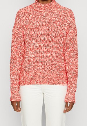 Pull en tricot rouge et blanc avec un col montant, coupe ample et poignets côtelés. La texture est épaisse, présentant un motif chiné.