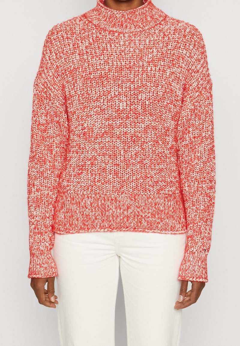 Červeno-bílý pletený svetr s vysokým límcem, volným střihem a žebrovanými manžetami. Textura je objemná a má melírovaný vzor.