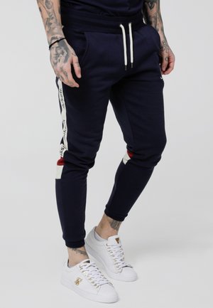 Navy joggers with a tapered fit, featuring white side stripes and red accents, made of soft fabric with drawstring waist and ribbed cuffs.