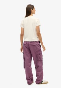 Paarse cargobroek met grote zijzakken, gemaakt van duurzaam stof. Gecombineerd met een lichtgekleurde blouse, met een ontspannen pasvorm en rechte pijpen.