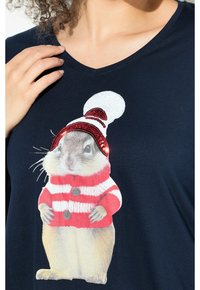 Nahaufnahme eines blauen Hemdes mit einem Eichhörnchen, das einen rot-weißen gestreiften Pullover und eine mit Pailletten besetzte Wintermütze trägt.