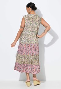 Robe maxi florale sans manches, avec un ourlet en couches dans des motifs roses et beiges, et des matériaux texturés. Des sandales compensées complètent le look.