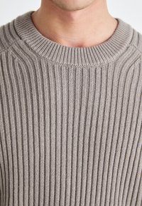 Grauer gerippter Strickpullover mit rundem Ausschnitt und strukturiertem Oberflächen, der vertikale Linien und ein weiches, angenehmes Erscheinungsbild zeigt.