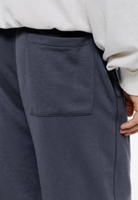 Navy joggingbroek met een gladde textuur en een zichtbare patchzak aan de rechterzijde. Heeft een elastische tailleband voor comfort.