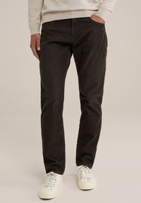 Crne kordurojske hlače ravnog kroja, s bočnim džepovima i suptilnom teksturom, uparene s bijelim tenisicama.