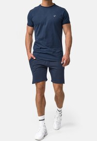 Dunkelblaues Baumwoll-T-Shirt mit rundem Halsauschnitt, kurzen Ärmeln und einem kleinen Logo auf der Brust, kombiniert mit passenden dunkelblauen Shorts.
