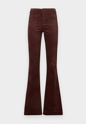 Jeans de pana marrón acampanados con cintura alta, que cuentan con cuatro bolsillos y una cremallera. Textura suave con estrías verticales.