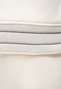 Gros plan d'une section de tissu beige avec une bande en maille texturée blanche et noire rayée au centre.