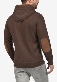 Bruine hoodie met een gestructureerde afwerking, een verstelbare capuchon en suède elleboogpatches. Mouwen en onderkant zijn aansluitend voor een veilige pasvorm.