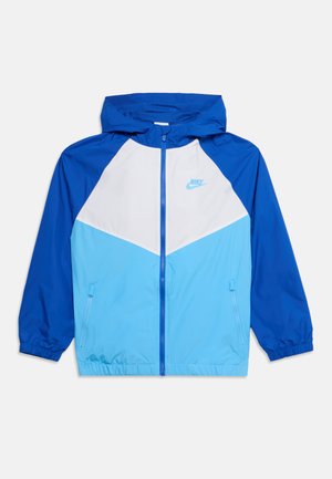 Veste coupe-vent à capuche Nike bleue et blanche avec une partie inférieure bleu clair, fermeture éclair frontale et poches latérales zippées.