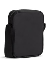 Συμπαγής μαύρη τσάντα χιαστί με μπροστινή πλευρά, χοντρό ρυθμιζόμενο λουρί και κορυφαίο φερμουάρ κλεισίματος, εμφανίζεται σε λευκό φόντο.