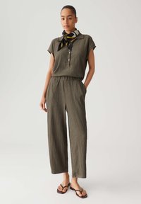 Olive green, textured two-piece outfit with a collared short-sleeve top and wide-leg trousers, paired with a patterned scarf and flip-flops.