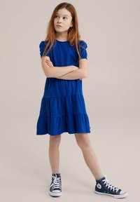 Blå bomulls klänning med flera lager och korta puffärmar, tillsammans med blå höga sneakers. Enkel design med texturerad tyg och rundad halsringning.