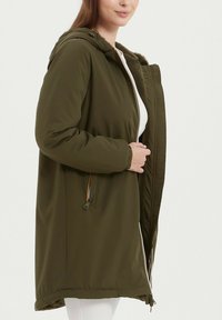 Parka vert olive avec fermeture éclair à l'avant, capuche et doublure en fourrure intérieure. Comprend des poignets élastiques et des poches latérales. Texture lisse et design décontracté.