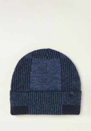 Gorro de patchwork tejido en azul oscuro y negro con secciones acanaladas y texturizadas y una pequeña etiqueta de tela de la marca en el puño.