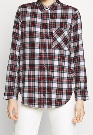 Chemise à carreaux rouge, blanche et noire à manches longues avec poche poitrine, portée par une personne debout, les bras relâchés le long du corps.