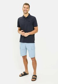 Marine polo shirt, lichtblauwe cargo shorts en zwarte sandalen. Het shirt heeft een kraag en een klein logo. De cargo shorts hebben zijzakken.