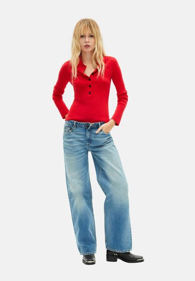 Rød ribstrikket langærmet top med henley-halsudskæring og sorte knapper, kombineret med løstsiddende lyseblå jeans og sorte hælede støvler.