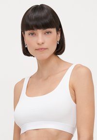 Valkoinen ribbikuvioitu bralette, jossa on leveä, pehmeä vyötärönauha ja leveät olkaimet. Miellyttävä pinta ja minimalistinen muotoilu, ilman näkyvää metalliosaa.