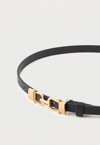 Fekete, vékony bőr öv arany színű, összekapcsolható csattal és állítható lyukakkal, fehér háttér előtt.