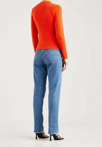 Pull orange côtelé à manches longues associé à un jean large bleu délavé et des sandales noires à talons, vu de dos.