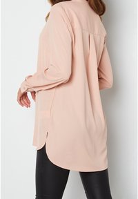 Bluse in hellrosa mit langen Ärmeln, einer geknöpften Manschette und einem abgerundeten Saum. Verfügt über Falten am Rücken und eine glatte, weiche Textur.