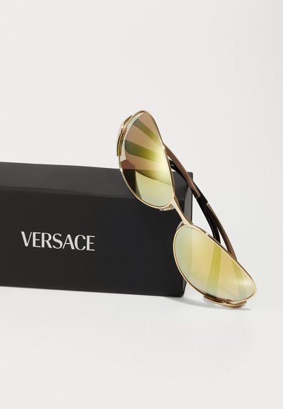 Kuldraamid päikeseprillid, millel on peegeldavad kollase-rohelised läätsed. Kaasas must ristkülikukujuline kott Versace logo jaotisega.