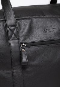 Black leather bag featuring pebbled texture, top stitching, a front zipper pocket, and a distinct logo embossed on the surface.