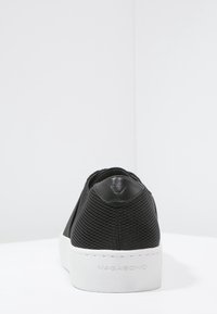 Baskets slip-on noires texturées avec semelle blanche, "VAGABOND" embossé au talon, photographiées sur fond blanc uni.