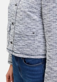 Gestructureerde geweven jack in wit en marineblauw met twee voorkezen en zilveren knopen, gecombineerd met een blauwe denim taille.