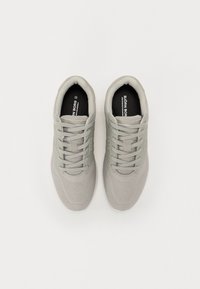 Baskets de sport gris clair avec tige en mesh, design texturé et accents renforcés. Présentent des lacets gris et une semelle intérieure noire avec une marque.