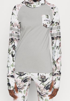 Graues Langarmshirt mit floral bedruckten Ärmeln und Tasche, kombiniert mit passenden floralen Leggings bei einer stehenden Person.