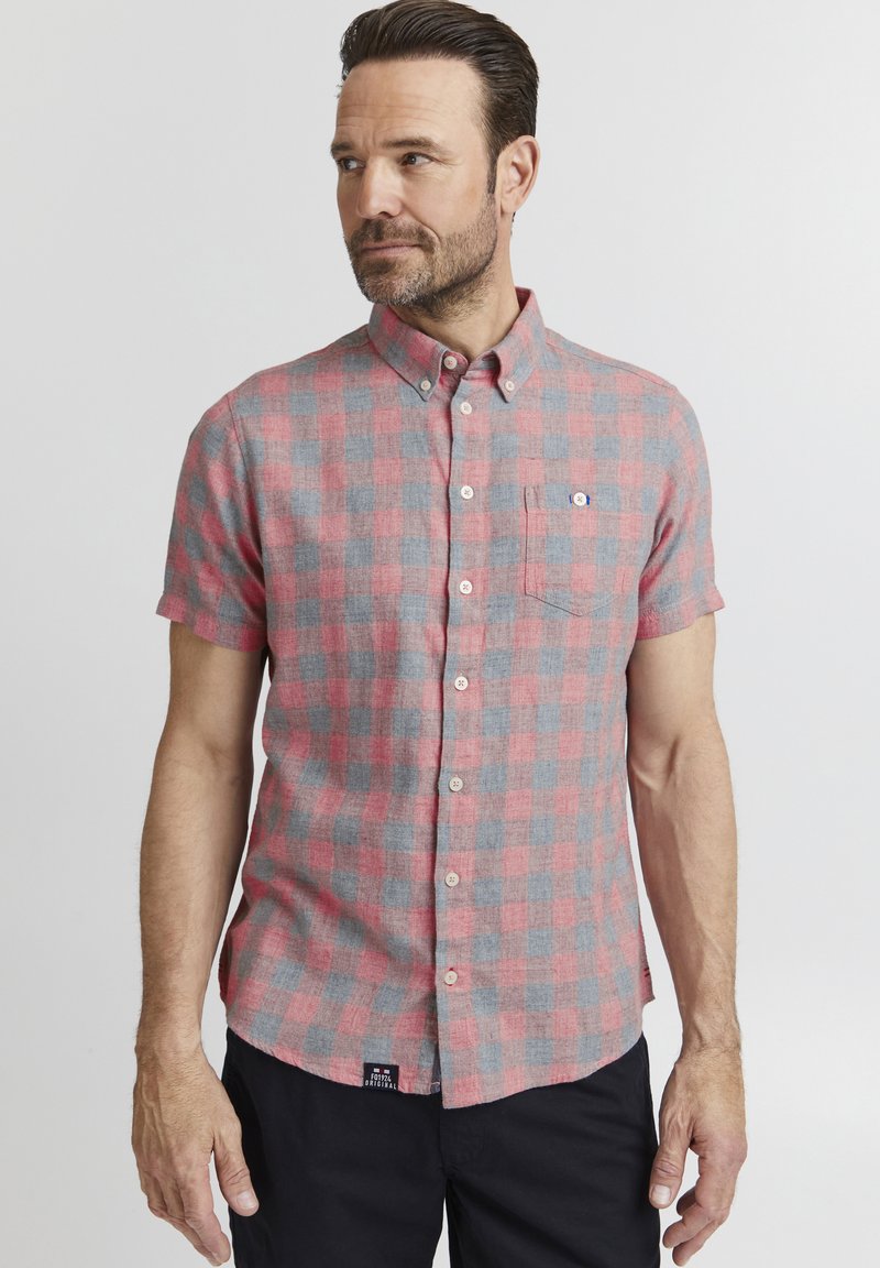 Camicia a maniche corte con bottoni in una fantasia a quadri rosa e grigia, il tessuto sembra avere una texture morbida, presenta una tasca sul lato sinistro del petto e un'etichetta sull'orlo.