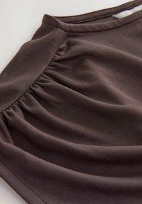 Tela marrón con textura arrugada, que presenta una superficie lisa y un acabado ligeramente elástico, capturada en un ángulo para resaltar el caído.