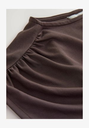 Barna textil, gyűrt szerkezettel, sima felülettel és enyhén ruganyos befejezéssel, melyet szögből örökítettek meg, hogy kihangsúlyozza a redőzést.