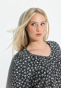 Blusa nera floreale con motivo a fiocco di neve bianco e dettagli in teal; presenta un collo a barca e maniche lunghe. Tessuto morbido e leggero.