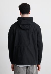 Sort hættejakke med en afslappet pasform, der har snor i hætten, elastiske manchetter og en glat, mat tekstur. Simpelt design.