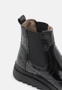 Botină din piele lăcuită neagră, cu panouri laterale elastice. Căptușeală texturată gri și o talpă proeminentă cu decupaje decorative.