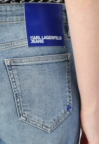Jasnoniebieskie dżinsy z denimu z prostokątną niebieską metką z napisem "KARL LAGERFELD JEANS". Posiadają tylnią kieszeń z detalami w szwie.