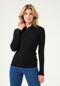 Black ribbed long-sleeve pullover with a zip neck and a collar. Fit is slim with a textured fabric, paired with blue jeans.