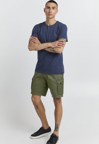 Mornarica majica s kratkim rukavima tipa henley s dva gumba, u kombinaciji s maslinasto zelenim cargo šortsevima koji imaju bočne džepove i ravni kroj.