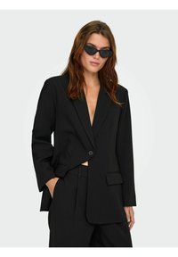 Sort skræddersyet blazer med en enkelt knaplukning, notch revers og to forlommer, parret med sorte cat-eye solbriller.