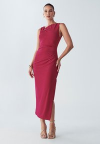 Pielāgots midi kleita dziļi magentas krāsā ar vienu plecu atsegumu, sānu krokojumu un augstu šķēlumu augšstilbā. Gluds, elastīgs audums un minimāla detalizācija.