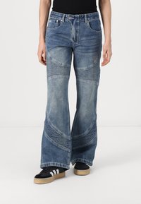 Jeans z razširjenimi hlačnicami iz denima v srednje modri barvi z teksturiranimi paneli in navpičnimi šivi, ki imajo visok pas in širok kroj.